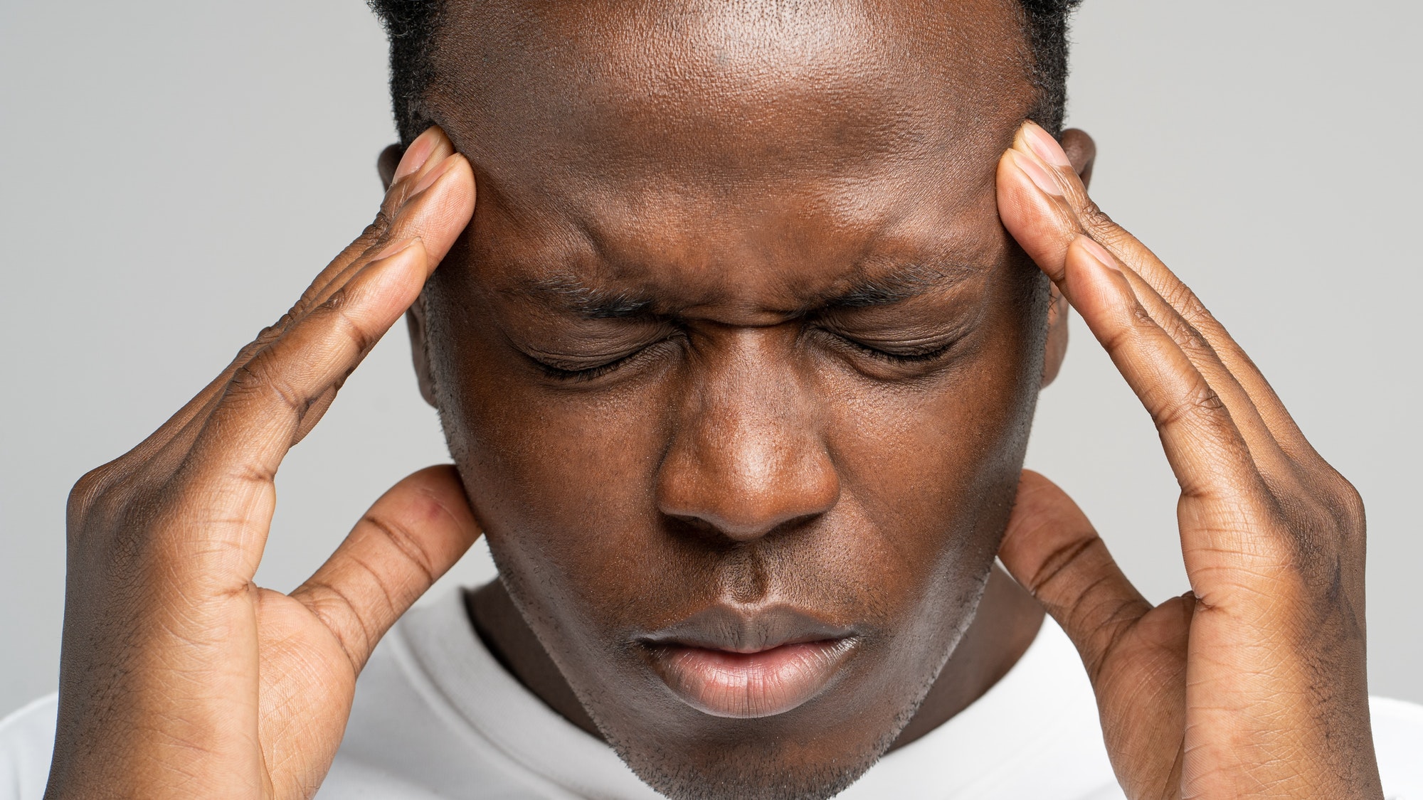 Exhausted upset African American man feeling pain suffering from migraine massaging temples. Studio.